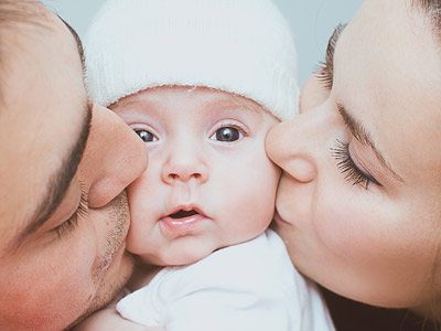 Ein Baby wird von zwei Eltern geküsst. Alle haben liebevolle Gesichtsausdrücke.
